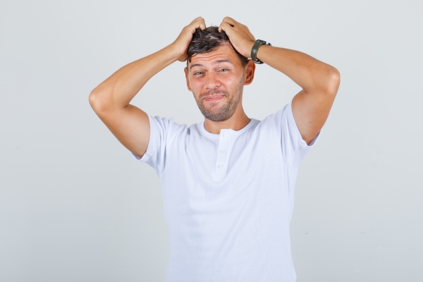 hombre blanco con polo sin cuello blanco echándose las manos a la cabeza preocupado por sus problemas capilares