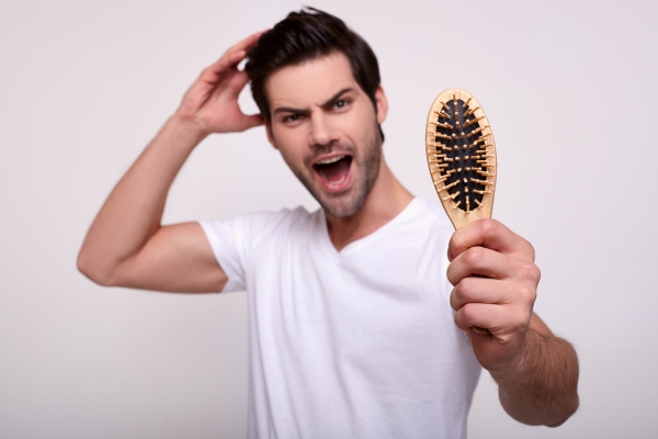 evitar la caída del cabello - hombre joven mostrando alegre el cepillo sin cabello tras haberse peinado
