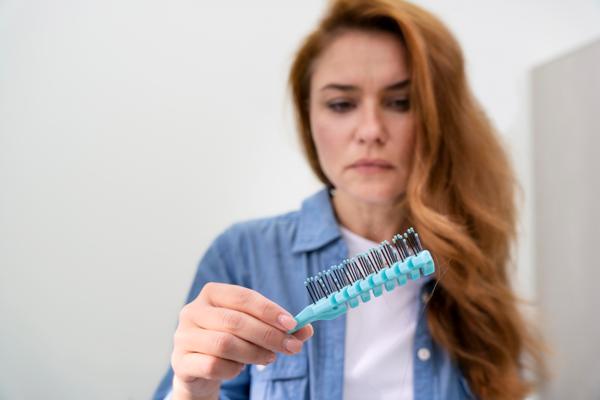 evitar la caída del cabello - mujer con el pelo cobrizo mirando el cepillo con preocupación por los cabellos que se han quedado en el