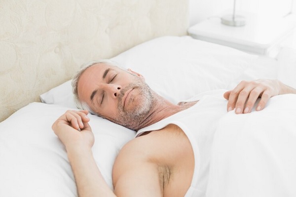 cómo dormir después de un implante capilar - hombre maduro con canas en la cabeza y la barba durmiendo boca arriba en la cama