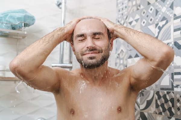 cómo dormir después de un implante capilar - hombre tomando una ducha con agua abundante