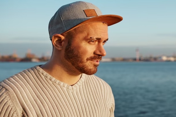 hombre joven con piercing y gorra a la orilla del mar