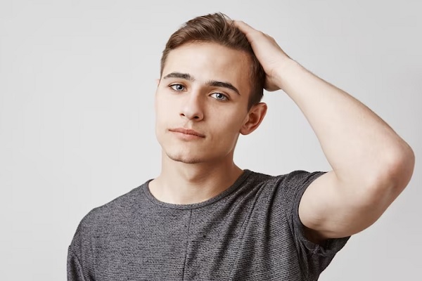 hombre joven con una camiseta de manga corta gris pasando la mano por su cabeza