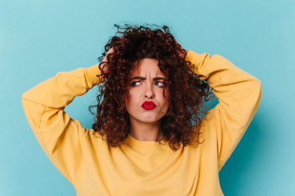Mujer con cabello rizado observando que comienza a perder hidratación en las puntas, debido a los factores externos que impactan directamente sobre la estructura capilar