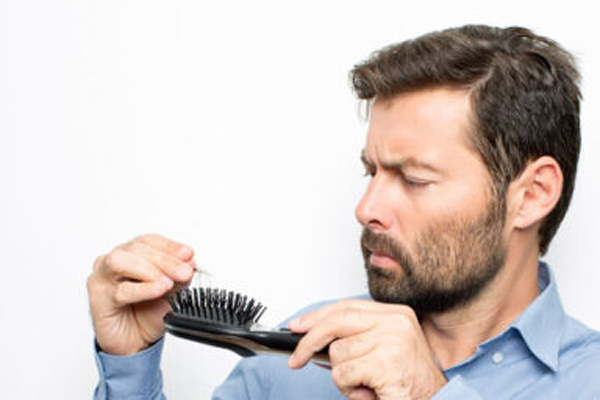 Por qué se nos cae mucho el pelo - Hombre observando que después de peinarse pierde más cabello de lo normal, como consecuencia de la alopecia androgénica