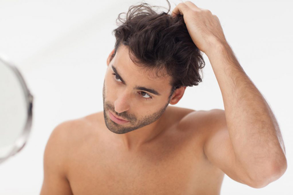 Hombre observando en el espejo como su cabello implantado crece de manera natural, recuperándose totalmente de la alopecia que padecía