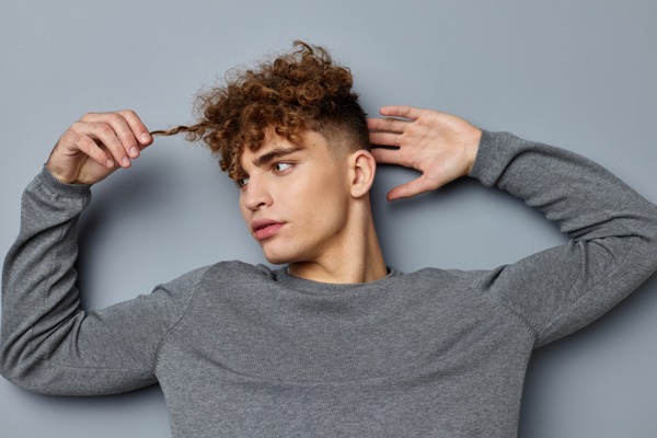 Lavarse el cabello todos los días - joven tumbado en el suelo estirando uno de los rizos de su cabello
