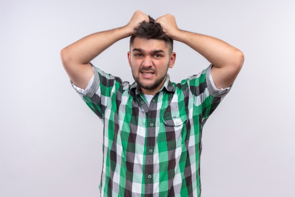 Joven con camisa de cuadros tira de su cabello desesperado ante altos niveles de rabia y estrés