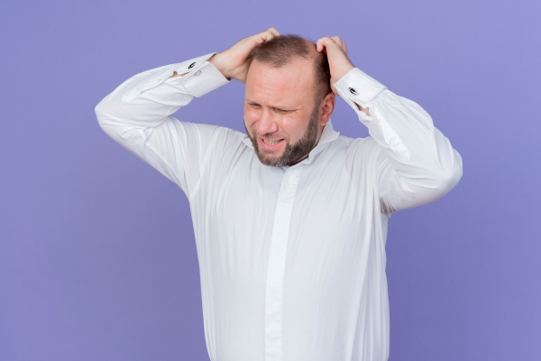 Alopecia nerviosa - hombre con camisa blanca llevándose las manos a la cabeza preocupado y con signos claros de sufrir alopecia