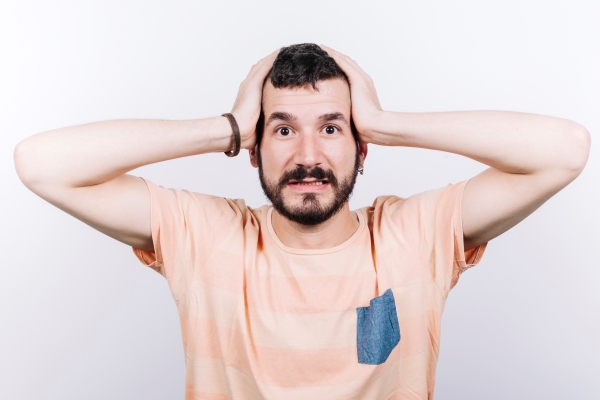 Tipos de entradas en el cabello - Hombre joven se lleva las manos a la cabeza en señal de preocupación por la pérdida sostenida de su pelo