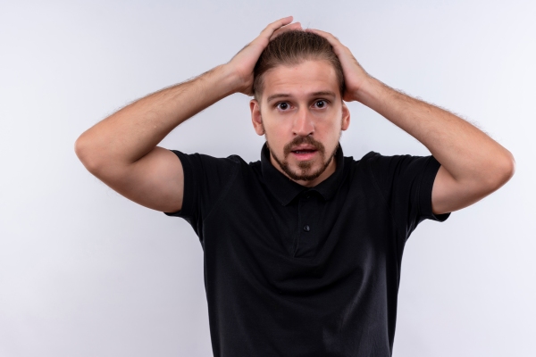 Tipos de entradas en el cabello - Joven de camisa negra se muestra sorprendido con los claros en el cuero cabelludo luego de peinar y llevar su melena hacia atrás