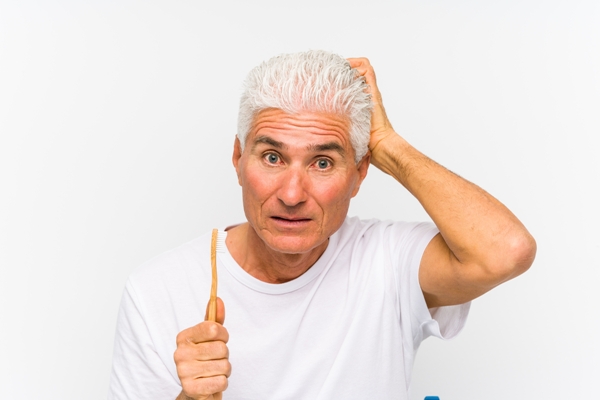 Adulto mayor con cepillo dental en mano se pregunta de dónde surgen los mitos sobre el cabello blanco 