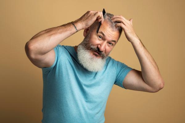 Hombre de barba canosa peina con detenimiento su pelo para evitar el desprendimiento innecesario de los folículos pilosos 