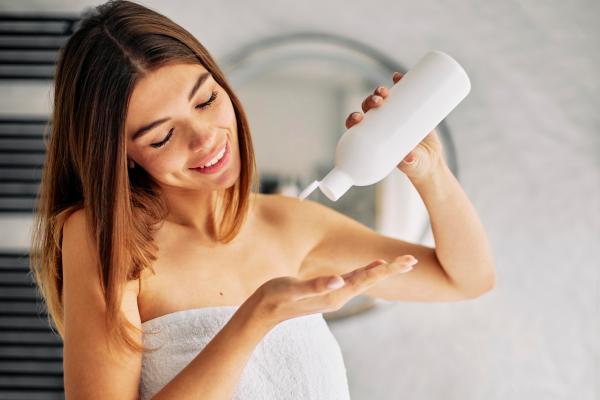 mujer en el baño con el bote de acondicionador en la mano preparándose para aplicarlo