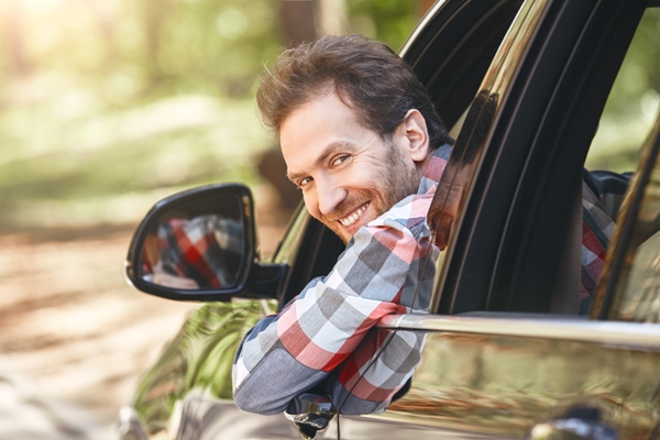 Tipos de entradas en el cabello - Hombre atractivo luce nuevo corte de pelo mientras saca la cabeza por la ventana de su auto