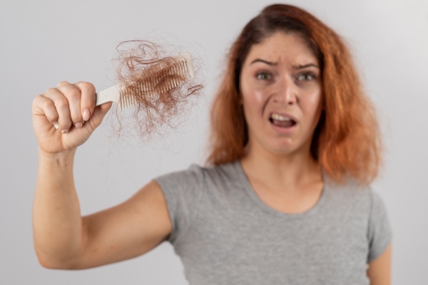 Alopecia nerviosa - mujer mirando preocupada el peine de su mano derecha que tiene un gran mechón de su cabello