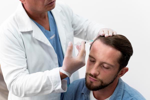 Médico especialista realizando un implante de pelo a un paciente masculino, para recuperar la densidad capilar afectada por la alopecia