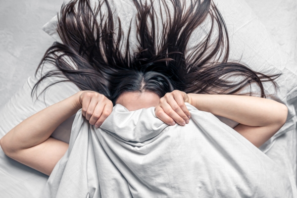 Dormir con el pelo mojado - mujer tumbada en la cama tapándose la cara con el edredón 