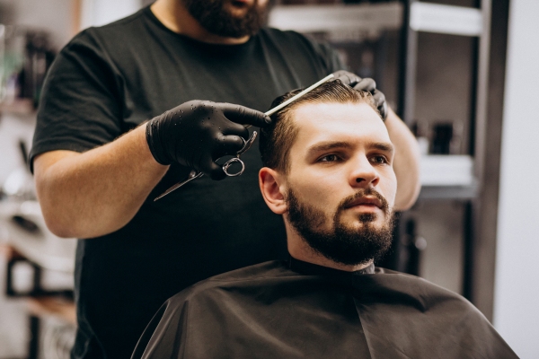 Cortes de pelo en el hombre - Estilista cortando el cabello de un hombre con rostro ovalado, al cual le resulta favorable todos los cortes de pelo