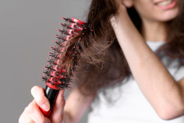 mujer tirando de su cabello con el cepillo para desenredarlo con cara de dolor