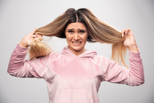 Duele el cabello - mujer con una sudadera rosa con capucha estirándose el cabello