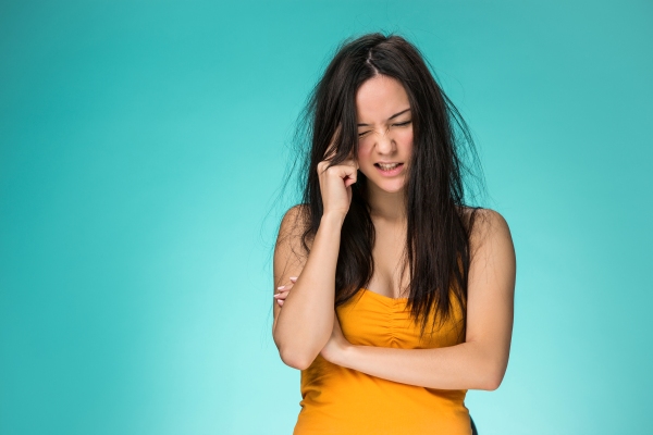 Dormir con el pelo mojado - mujer con el pelo con frizz con la mano en la sien y gesto de dolor