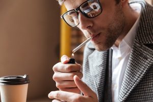 fumar aumenta la caída del pelo - hombre sentado en una cafetería encendiéndose un cigarro
