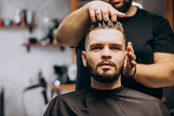 Barbero creando un estilo de peinado con capas a un cliente de rostro cuadrado, el cual permite equilibrar la anchura de la mandíbula