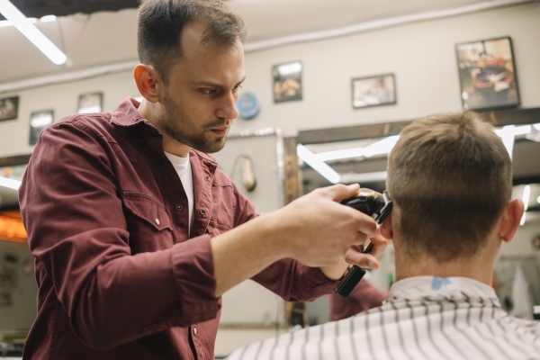 Barbero cortando el cabello de un cliente masculino con rostro diamante, para crear un estilo a media melena que permita realzar sus rasgos faciales y hacerlo lucir más atractivo