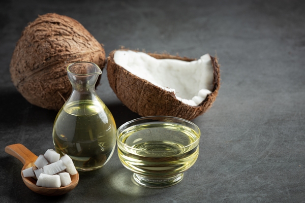 Aceite de coco en el pelo - aceite de coco en un bol y una aceitera con trozos de coco, un coco partido y uno entero