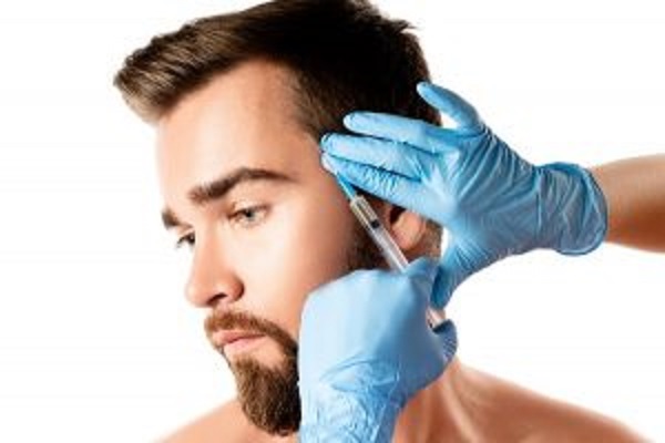 mesoterapia capilar - hombre en la consulta de la especialista la cual sostiene una inyección para realizar el tratamiento de mesoterapia capilar
