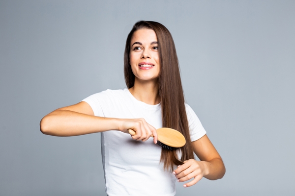 Aceite de coco en el pelo - mujer cepillándose su larga melena con cara de felicidad