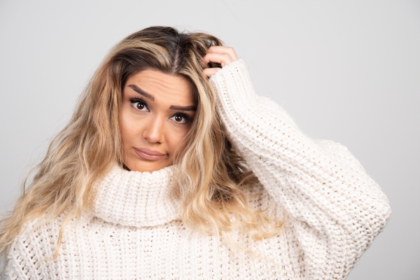 Duele el cabello - mujer con un jersey de cuello vuelto rascándose la cabeza