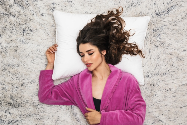 Dormir con el pelo mojado - mujer durmiendo sobre una manta de pelo con una bata rosa y la cabeza apoyada en una almohada