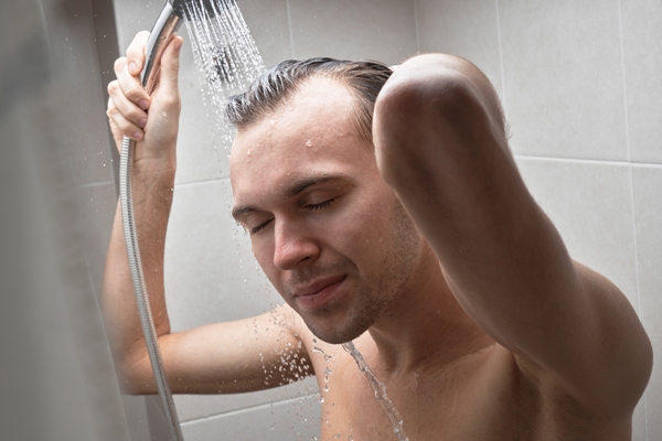Hombre lavando su cabello con una regadera suave, para no ocasionar daño a los folículos pilosos