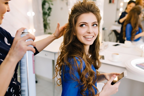 Estilista aplicando fijador al cabello de una clienta femenina, para aportar volumen y hacerla lucir atractiva
