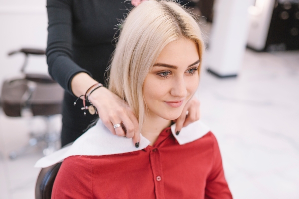 Estilista arreglando el cabello teñido de una clienta femenina, para hacerla lucir atractiva