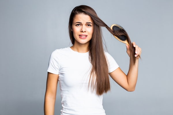 mujer joven con camiseta blanca cepillándose el pelo con cara de dolor