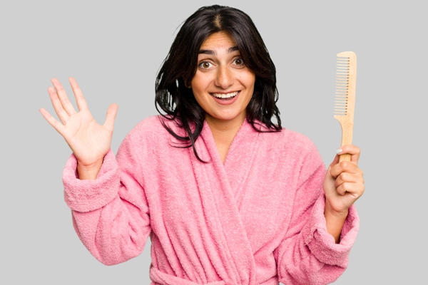 Mujer posando con un cepillo de dientes anchos, el cual permite desenredar el cabello sin ocasionar daño a las hebras capilares durante el peinado