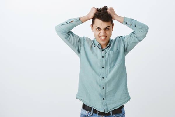 Duele el cabello - hombre joven con camisa y jeans agarrándose el cabello con cara de dolor