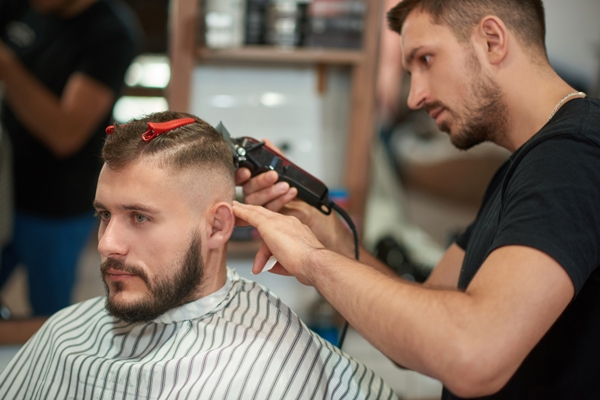 Estilista cortando el cabello de un cliente masculino con rostro triangular, creando un peinado de flequillo para disimular la anchura de la frente