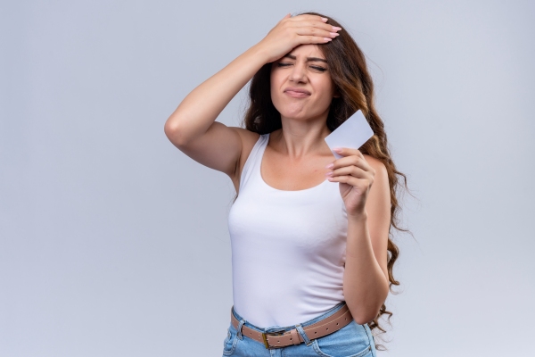 Dormir con el pelo mojado - mujer con camiseta blanca de tirantes y jeans con la mano en la cabeza y cara de dolerle la cabeza