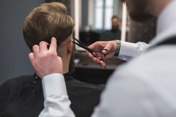 Cortes de pelo en el hombre - Barbero cortando el cabello de un cliente masculino con tijeras, para crear un estilo acorde a sus rasgos faciales y hacerlo lucir más atractivo