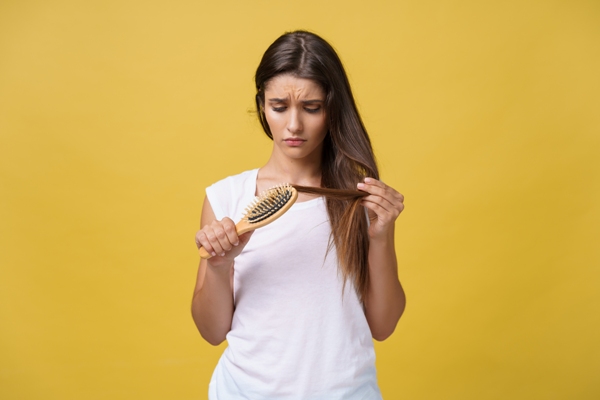 mujer joven mirando con preocupación su cabello mientras los cepilla