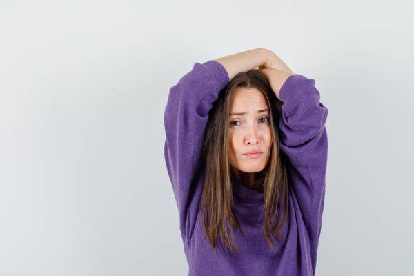 Dormir con el pelo mojado - mujer con jersey morado llevándose los brazos a la cabeza con gesto de dolor