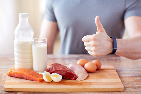 Cuidar el pelo en los hombres - Hombre haciendo un gesto positivo junto a diversos alimentos que contribuyen a mejorar la salud capilar