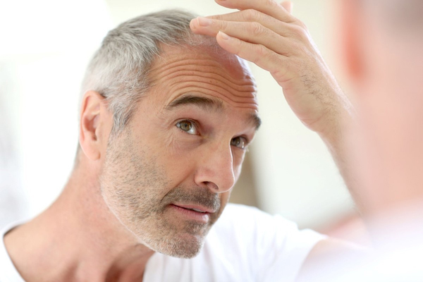 Cómo envejece nuestro pelo - Hombre observando frente al espejo el cabello con canas debido al envejecimiento prematuro del pelo