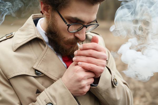 hombre encendiéndose un cigarro mientras el humo de alrededor contiene una calavera