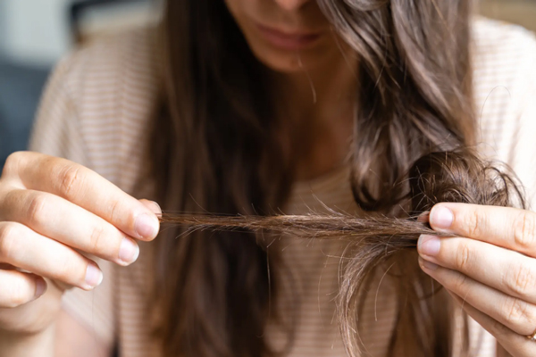 Cómo envejece nuestro pelo - Mujer sosteniendo en sus manos un mechón de pelo seco debido al envejecimiento del cabello por una rutina capilar inadecuada