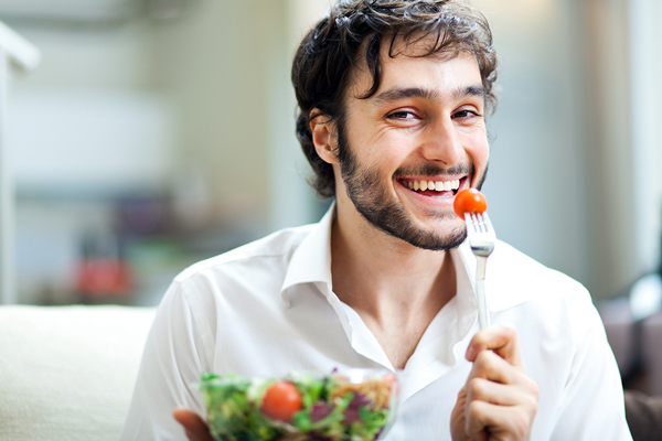 Fumar aumenta la caída del pelo - hombre sonriendo mientras se come un ensalada